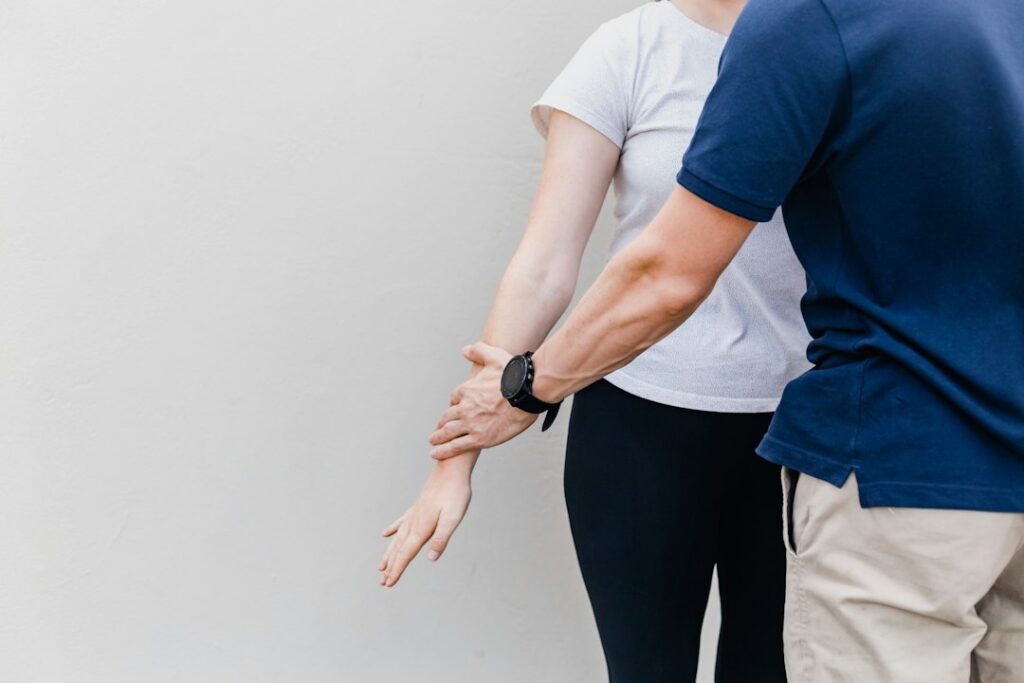 Adult performing gentle mobility exercises beside a treatment table in a bright, clean room.